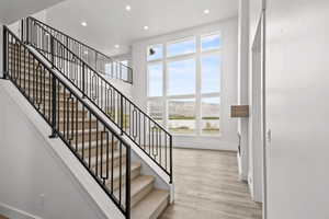 Stairway with plenty of natural light, light wood-type flooring, and a towering ceiling