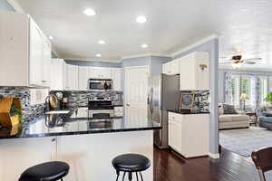 Kitchen with peninsula island , appliances with stainless steel finishes, backsplash, painted cabinets, corner pantry, and wood flooring.