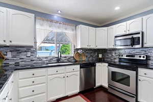 Kitchen with peninsula island , appliances with stainless steel finishes, backsplash, painted cabinets, corner pantry, and wood flooring.