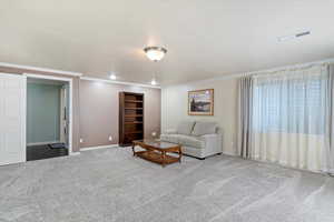 Carpeted basement family room featuring a textured ceiling, crown molding and can lighting.