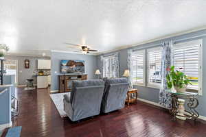 Spacious family room featuring ceiling fan, a textured ceiling, hardwood floors, plantation shutters and crown molding.