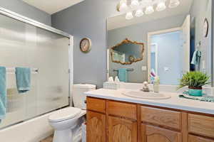 Full bathroom with vanity, a textured ceiling, enclosed tub / shower combo, and toilet.