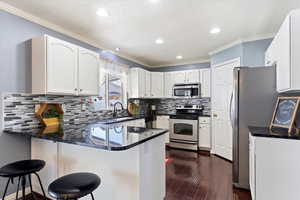 Kitchen with peninsula island , appliances with stainless steel finishes, backsplash, painted cabinets, corner pantry, and wood flooring.