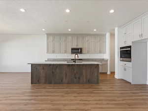 Kitchen with a kitchen island with sink, hardwood / wood-style floors, a textured ceiling, light stone countertops, and appliances with stainless steel finishes