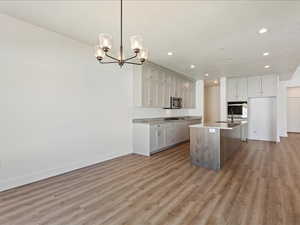 Kitchen with a center island with sink, appliances with stainless steel finishes, hanging light fixtures, sink, and hardwood / wood-style flooring