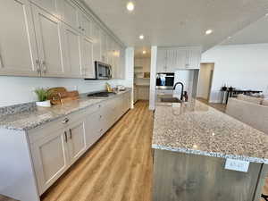 Kitchen with stainless steel appliances, a textured ceiling, sink, and light hardwood / wood-style flooring