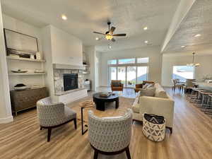 Living room with light hardwood / wood-style floors, ceiling fan with notable chandelier, and a textured ceiling