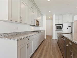 Kitchen featuring light stone countertops, stainless steel appliances, sink, white cabinetry, and hardwood / wood-style flooring