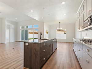 Kitchen featuring light hardwood / wood-style flooring, an island with sink, stainless steel appliances, sink, and light stone counters