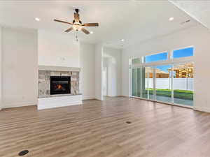 Unfurnished living room with a stone fireplace, ceiling fan, and light hardwood / wood-style flooring