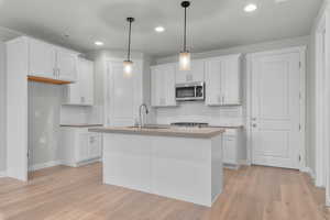 Kitchen with white cabinetry, a kitchen island with sink, light hardwood / wood-style flooring, pendant lighting, and sink