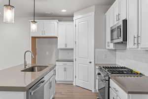 Kitchen with sink, pendant lighting, light wood-type flooring, white cabinetry, and appliances with stainless steel finishes