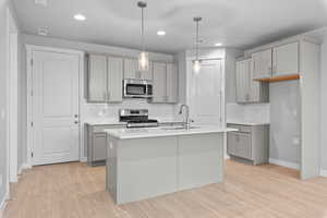 Kitchen with gray cabinetry, sink, light hardwood / wood-style floors, stainless steel appliances, and a center island with sink