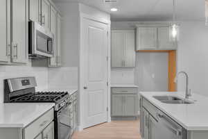 Kitchen with light hardwood / wood-style flooring, stainless steel appliances, backsplash, sink, and decorative light fixtures