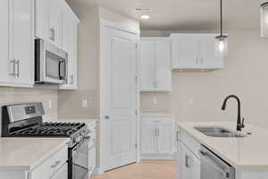 Kitchen featuring white cabinetry, stainless steel appliances, hanging light fixtures, and sink