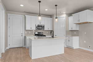 Kitchen with appliances with stainless steel finishes, sink, an island with sink, hanging light fixtures, and white cabinetry