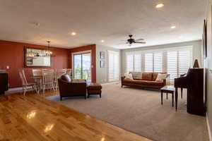 Living room featuring ceiling fan with notable chandelier, a textured ceiling, and hardwood / wood-style flooring