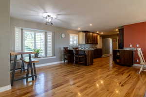 Kitchen featuring a kitchen bar, dark brown cabinets, kitchen peninsula, light stone counters, and light hardwood / wood-style floors