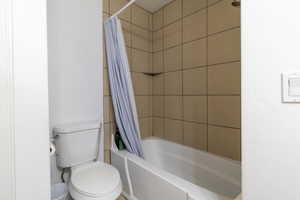 Bathroom featuring toilet and shower / bathtub combination with curtain