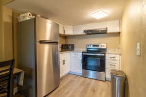 Kitchen with white cabinetry, stainless steel appliances, light stone countertops, and light wood-type flooring