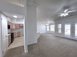 Unfurnished living room with light carpet, crown molding, french doors, and ceiling fan