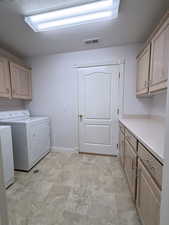 Laundry area with separate washer and dryer, cabinets, and light tile patterned floors