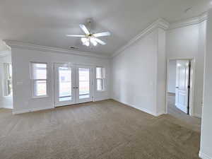 Carpeted spare room featuring ceiling fan, french doors, a wealth of natural light, and ornamental molding