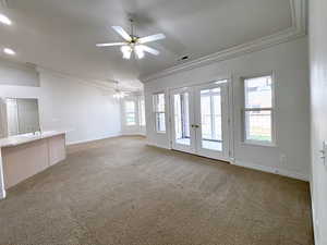 Unfurnished living room with crown molding, carpet, ceiling fan, and french doors