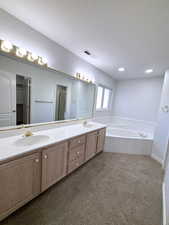 Bathroom with a tub to relax in, a textured ceiling, and dual bowl vanity