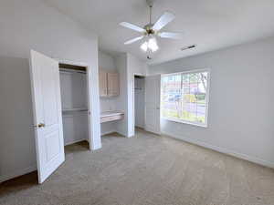 Unfurnished bedroom featuring two closets, light colored carpet, lofted ceiling, and ceiling fan