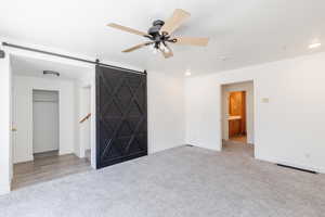 Unfurnished room with ceiling fan, a barn door, and light colored carpet