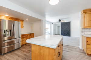 Kitchen with ceiling fan, decorative backsplash, stainless steel fridge with ice dispenser, light carpet, and a center island