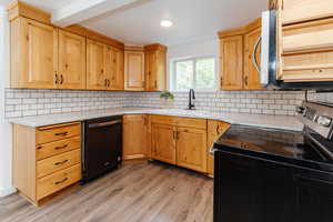 Kitchen with light wood-type flooring, sink, range with electric stovetop, black dishwasher, and backsplash