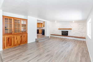 Unfurnished living room featuring a stone fireplace, light wood-type flooring, and a textured ceiling