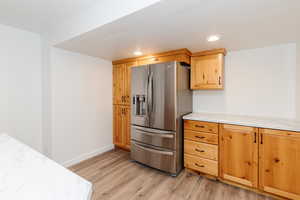 Kitchen with stainless steel fridge with ice dispenser, light hardwood / wood-style floors, and light stone counters