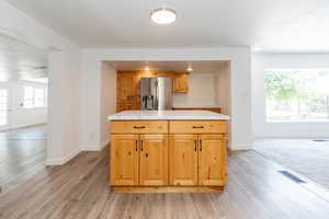 Kitchen with stainless steel refrigerator with ice dispenser, a center island, tile counters, and light wood-type flooring