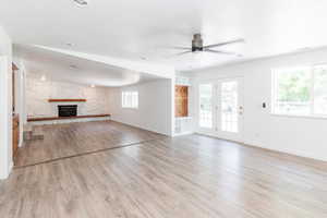 Unfurnished living room with light hardwood / wood-style floors, a healthy amount of sunlight, and a stone fireplace