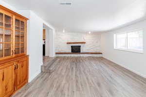 Unfurnished living room featuring a stone fireplace, a textured ceiling, and light hardwood / wood-style flooring