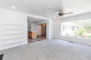 Unfurnished living room with dark carpet and ceiling fan