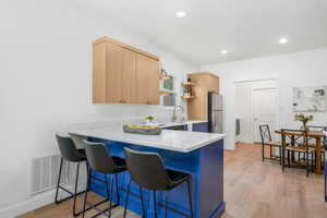 Kitchen with light brown cabinetry, a kitchen bar, stainless steel fridge, light hardwood / wood-style floors, and kitchen peninsula