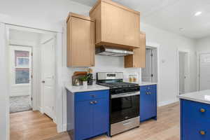 Kitchen featuring stainless steel gas range, light brown cabinetry, blue cabinetry, and light hardwood / wood-style floors