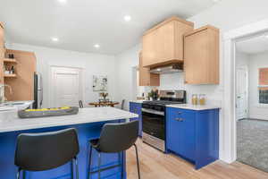 Kitchen featuring appliances with stainless steel finishes, a breakfast bar area, light colored carpet, and light brown cabinets