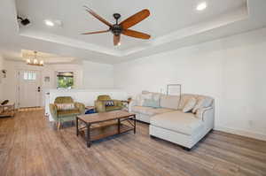 Living room with ceiling fan with notable chandelier, a tray ceiling, and hardwood / wood-style flooring