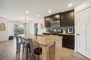 Kitchen featuring stainless steel appliances, hanging light fixtures, decorative backsplash, sink, and light stone counters