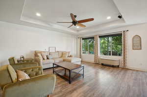 Living room featuring ceiling fan, wood-type flooring, and a tray ceiling