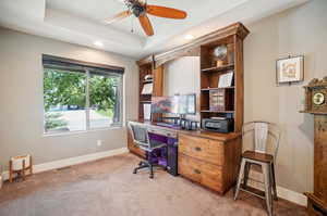 Office space with a raised ceiling, light colored carpet, and ceiling fan