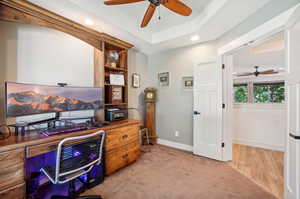 Carpeted home office featuring a tray ceiling and ceiling fan