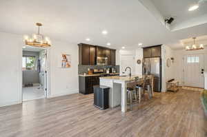 Kitchen with stainless steel appliances, light hardwood / wood-style floors, decorative light fixtures, and a center island with sink