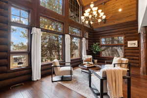 Interior space with rustic walls, dark hardwood / wood-style floors, high vaulted ceiling, a chandelier, and wood ceiling