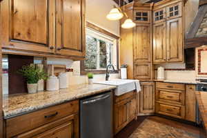 Kitchen with light stone countertops, stainless steel dishwasher, pendant lighting, backsplash, and sink